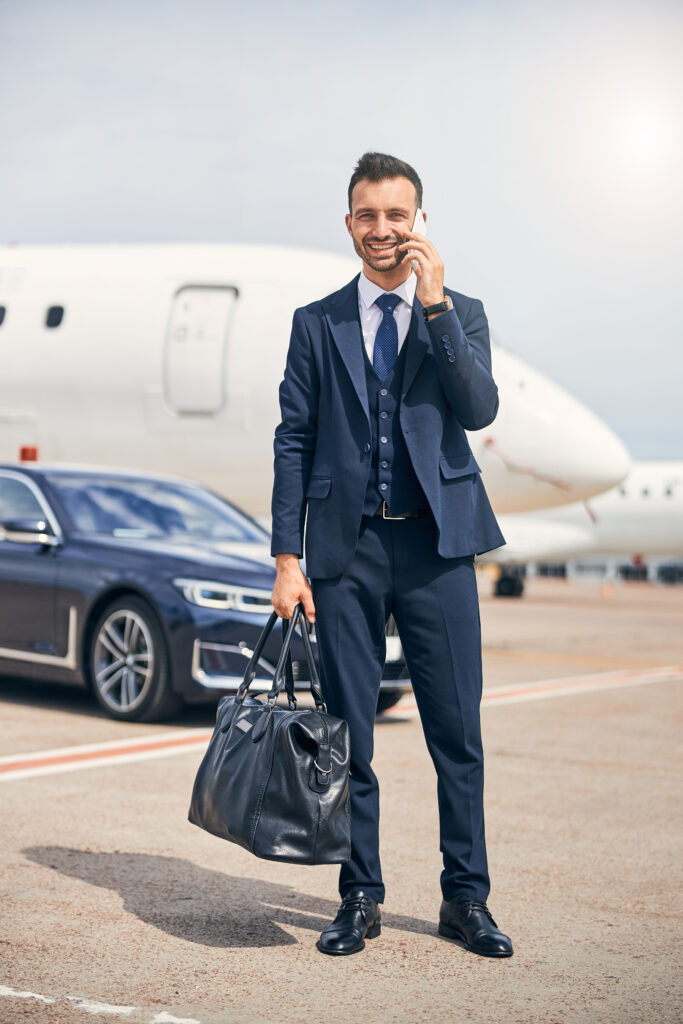 Successful man looking business-like holding a duffel bag standing in front of an airplane