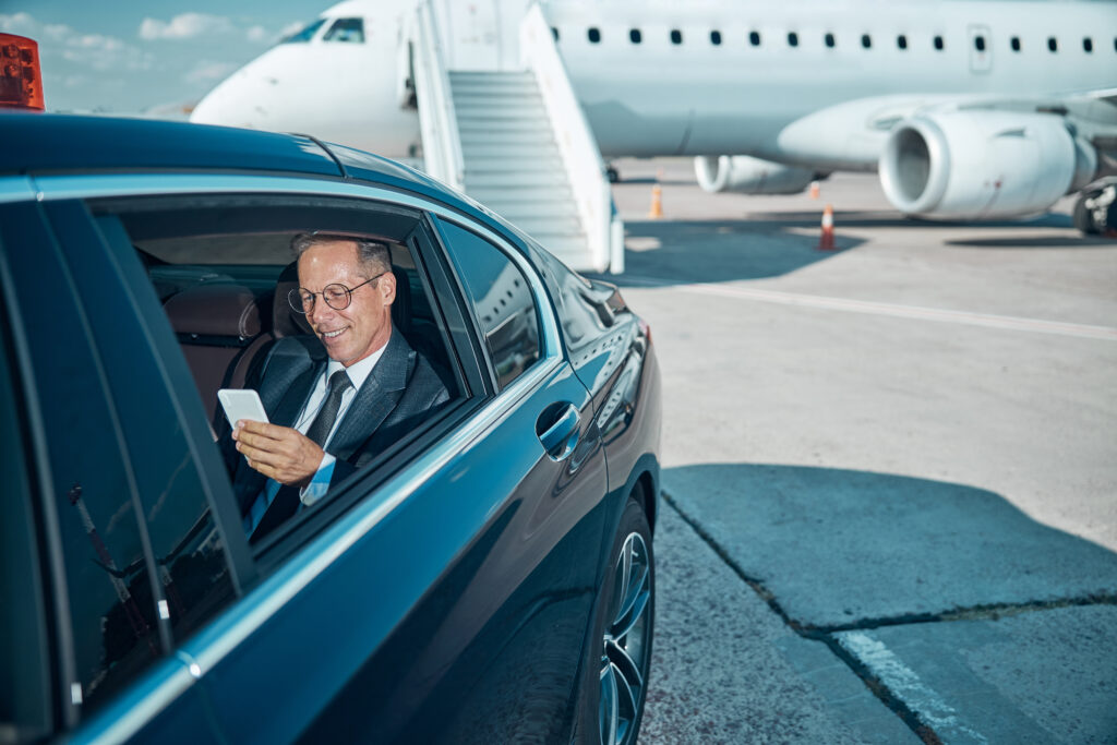 Cheerful businessman with smartphone in car at airport
